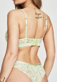 Lichtgroene kant lingerie set met een bloemdesign, verstelbare bandjes en een haak-en-oogsluiting aan de achterkant.