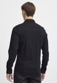 Fekete, hosszúujjú ing klasszikus gallérral, gombos mandzsettákkal és sima, elegáns textúrával. A hátsó nézeten látható a testhez simuló fazon és a varrási részletek.