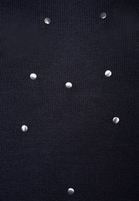 Schwarzer Strickstoff mit kreisförmigen silbernen Nieten, die in einem Muster angeordnet sind und der Oberfläche Textur und Kontrast verleihen.