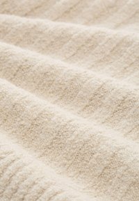 Zacht beige textiel met een subtiele verhoogde structuur, wat een luxe en gezellige uitstraling geeft. Ideaal voor dekens of stoffering.