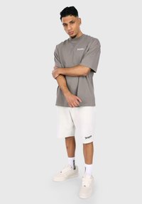 Szürke, oversize póló "Dropsize" logóval, fehér texturált rövidnadrággal és fehér sportcipővel párosítva. Kényelmes fazon, laza dizájn.
