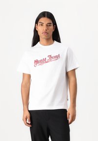 Hvit bomull t-skjorte med en rød "Guess Jeans" logo over brystet, kort erm, og løs passform. Glatt tekstur og klassisk design.