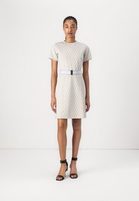 Robe beige à manches courtes avec un motif texturé et une taille ornée d'une boucle métallique. Des sandales à talons hauts noires complètent le look.