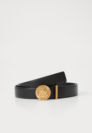 Ceinture en cuir noir avec une boucle circulaire dorée arborant un emblème de lion, un bord texturé et une finition lisse. Longueur ajustable.