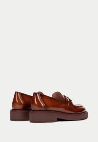 Bruine leren loafers met een glanzende afwerking, voorzien van een vierkante neus en een kleine blokhak. Accenten in goudkleurig metaal benadrukken de voorkant.