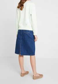 Mátově zelená mikina, džínová sukně do A s rozparkem na zádech, béžové nazouvací boty. Ležérní outfit s jednoduchým designem a pohodlným střihem.