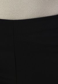 Svarta åtsittande byxor med en slät textur, med en minimalistisk design och en subtil söm fram. Överdel i beige stickad.
