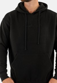 Felpa nera con tessuto testurizzato, cordini e tasca frontale. Caratterizzata da un sottile testo "Project x" dello stesso colore.