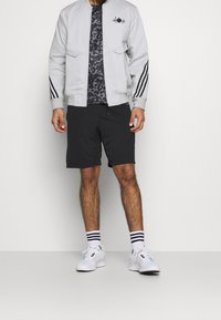 Gray bomber jacket with black accents, patterned T-shirt, black shorts, and white sneakers with colorful details; horizontal stripes on socks.