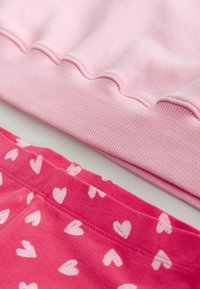 Suéter de color rosa claro con textura acanalada, combinado con pantalones cortos de color rosa brillante con un patrón de corazones blancos. Ambos están hechos de tela suave.