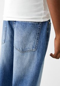 Ljusblå denimjeans med lös passform, med två bakfickor och en slät textur, i kombination med en vit ribbad linne.