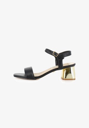 Sandal de cuero negro con punta cuadrada, tira en el tobillo, detalle de hebilla dorada y tacón bloque geométrico transparente. Textura suave.