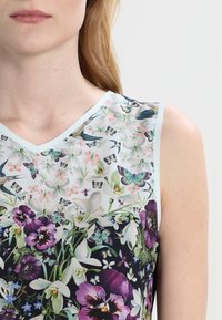 Květinový top bez rukávů s V-výstřihem. Materiál má světle modrý okraj s živým potiskem motýlů a květin.