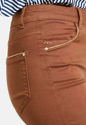 Jeans marroni con una texture liscia, caratterizzati da una tasca laterale con una cerniera decorativa e tre borchie sopra la tasca.