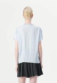 Blusa azzurra a maniche corte con un motivo testurizzato e scollatura arricciata, abbinata a una gonna plissettata scura.