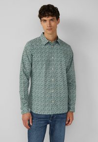 Chemise à manches longues verte avec un motif floral, fermeture à boutons sur le devant et un col classique. Le tissu semble léger avec une texture lisse.
