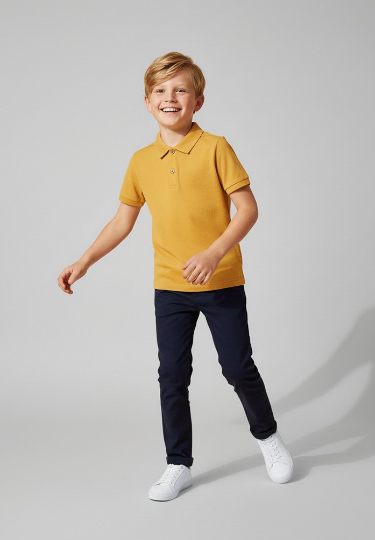 Żółta koszulka polo z zapięciem pod szyją, w połączeniu z ciemnoniebieskimi spodniami i białymi trampkami. Ubrania mają luźny krój i gładką teksturę.