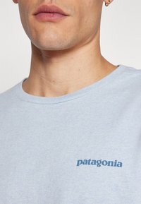 Světlemodré bavlněné tričko s krátkými rukávy a kulatým výstřihem. Na levé straně hrudi se nachází tmavěmodré logo "patagonia".
