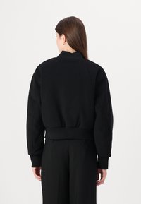 Giacca bomber nera corta con colletto e polsini a coste. Tessuto morbido, vestibilità oversize e dettagli di cucitura sottili sulle spalle.