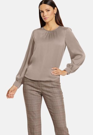 Langarmige, taupe blouse met een ronde halslijn, geplooide details aan de voorkant en zachte draping. Gecombineerd met een geruite broek.