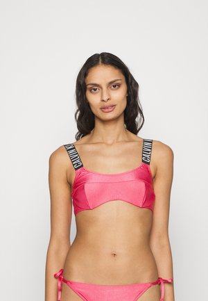 Bikini crop top en tissu côtelé rose vif. Dispose de larges bretelles noires avec texte blanc, d'un col carré et d'une coupe ajustée.