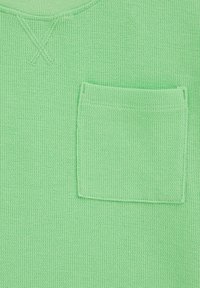 Gaiši zaļš adīts džemperis ar apaļu kakla izgriezumu un krūšu kabatu. Audums ir vaļīgs un elpojošs, ar maziem vertikāliem riņķiem.