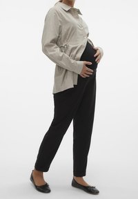 Maternity shirt in light striped fabric with a tie waist, paired with black tapered pants and black flats. Model cradles her belly.