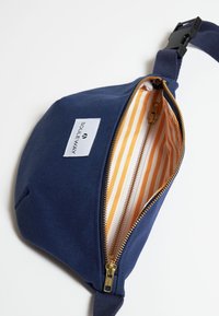 Riñonera de tela azul marino con un cierre dorado. El interior presenta un forro de rayas amarillas y blancas. Incluye una etiqueta de marca en el exterior.