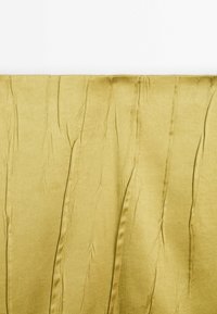 Tissu en satin jaune avec des plis et des rides verticales visibles, présenté sur un fond blanc uni.