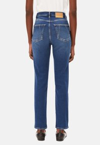 Jeans en denim bleu taille haute avec une coupe droite, deux poches arrière et une étiquette en cuir carré sur la ceinture. Texture lisse, design classique.