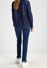 Mörk denimjacka med knäppdesign, kombinerad med blå skinny jeans och vita sneakers. Har vända ärmar och en avslappnad passform.