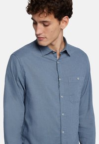 Camicia blu a maniche lunghe in tessuto leggero con colletto abbottonato, tasca anteriore e finitura testurizzata; dotata di bottoni chiari.