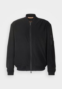 Černá bomber bunda se zapínáním na zip, žebrovaným límcem a manžetami a zipovou kapsou na levém rukávu. Hladká tkanina s minimálními detaily.