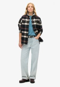 Fleece-skjorte i sort og hvidt tern, lagd over en blå top, parret med lyseblå jeans og sorte loafers. Afslappet pasform i denim.