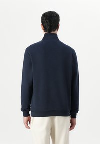 Mornarsko flis pulover z visokim ovratnikom, dolgimi rokavi ter rebrastimi manšetami in robom. Mehka tekstura z minimalnim dizajnom in brez vidne blagovne znamke.