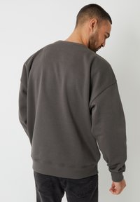 Grå sweatshirt med en afslappet pasform, ribbede manchetter og nederste kant, lavet af blødt materiale med et rent, minimalt design.