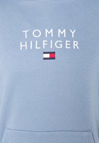 Sudadera azul claro hecha de algodón, con el texto bordado en blanco "TOMMY HILFIGER" y un pequeño parche de logo en rojo, blanco y marino.