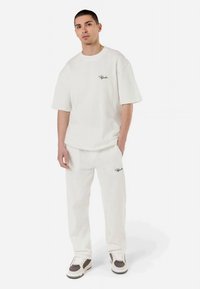 T-shirt branca de algodão com ribas, de mangas curtas e com decote careca, combinada com calças a condizer que apresentam uma marca bordada em preto.