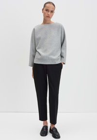 Grijze trui met een botte halslijn en lange mouwen, gecombineerd met strakke zwarte broeken en zwarte instappers. Eenvoudig ontwerp, zachte textuur.