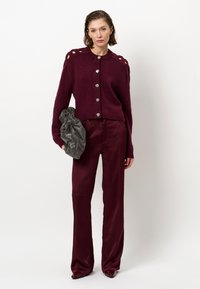 Bordeaux gebreide cardigan met zilveren knopen, met uitgesneden schouderdetails. Gecombineerd met bijpassende bordeaux broek en een grijze clutch tas.