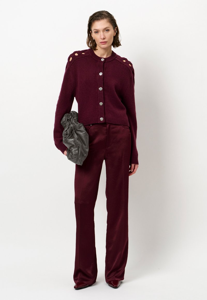Bordeaux gebreide cardigan met zilveren knopen, met uitgesneden schouderdetails. Gecombineerd met bijpassende bordeaux broek en een grijze clutch tas.