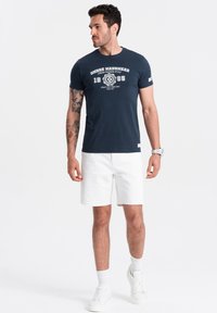 Navy blue short-sleeve t-shirt with white graphic text, paired with white shorts. Features a round neckline and a fitted design.