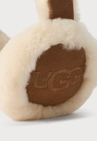 Lurvete beige ørevarmere med innermembran i brunt semsket skinn og "UGG" brodert på ørekoppen.