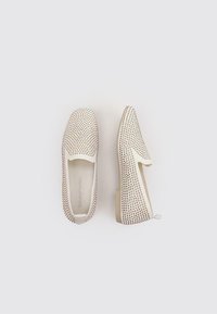 Zapatillas blancas sin cordones con un diseño perforado, que presentan una textura suave, un tacón bajo y acentos minimalistas.