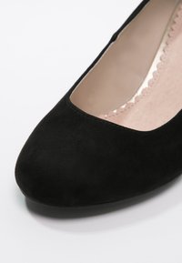 Chaussure plate en daim noir à bout fermé avec doublure intérieure beige festonnée, vue en gros plan et en angle par le dessus.