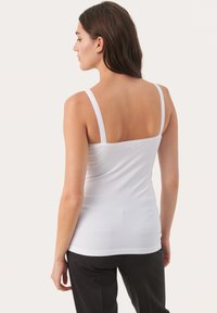 Vit ärmlös topp i stretchigt material. Har tunna remmar och en figurnära design, slät textur och en enkel, ren silhuett.