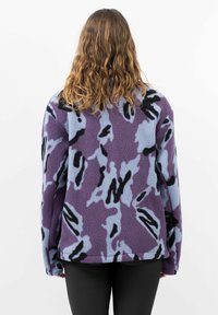 Fleece jas in paars, lichtblauw en zwart camouflagedessin. Boxy vorm met lange mouwen, zachte textuur en een licht gebogen zoom.