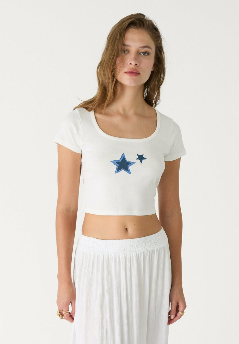 Hvid cropped t-shirt med rund halsudskæring, prydet med blå stjernebroderi foran. Blødt bomuldsstof, korte ærmer og afslappet pasform.