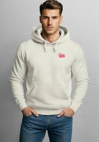Hellbeige Kapuzenpullover mit einer frontalen Tasche und Kordelzugkapuze; mit rotem "Social Beach"-Logo auf der linken Brust. Kombiniert mit blauen Jeans.