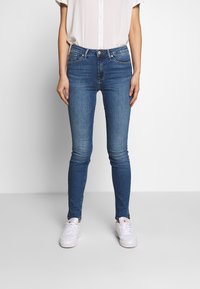 Dunne blauwe jeans met een gemiddelde wassing, gemaakt van denim. Bevat een knoop- en ritssluiting, vijf zakken en heeft een soepele textuur.